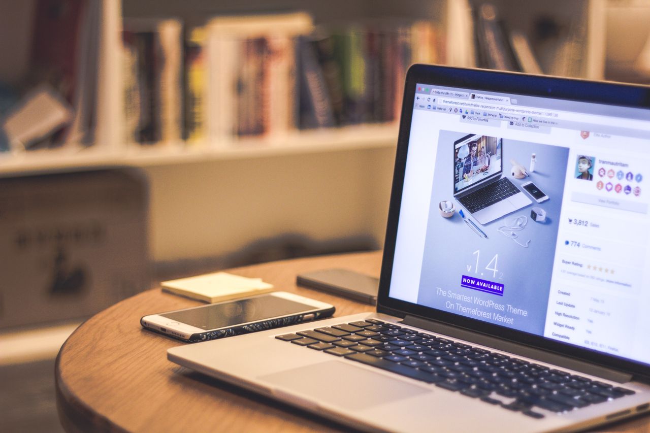 Un espace de travail moderne et chaleureux avec un ordinateur portable affichant un site web, un smartphone et des livres sur des étagères.